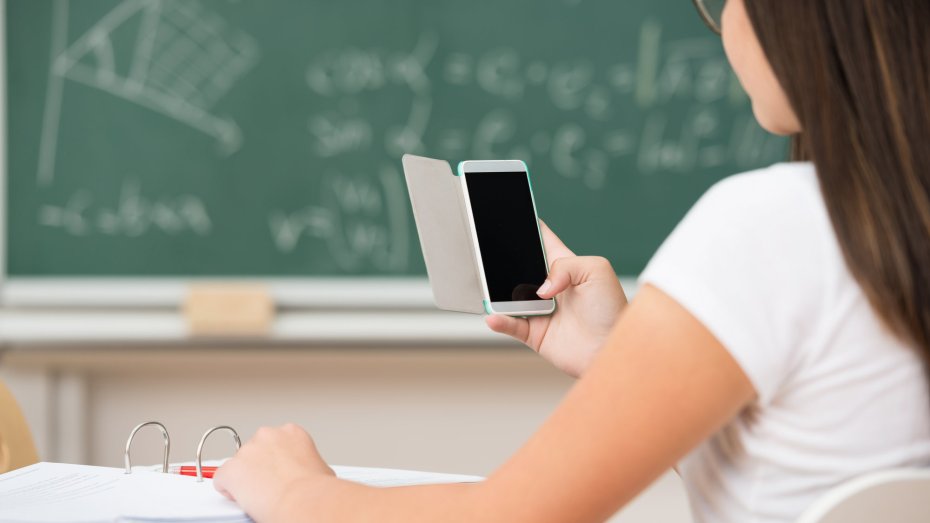 Symbolbild: Schülerin im Klassenraum mit Handy in der Hand