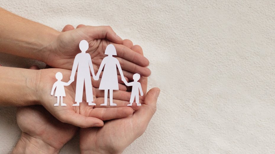 Symbolbild: Gefaltete Hände, die ausgeschnittene Figuren einer Familie aus Vater, Mutter, zwei Kindern halten