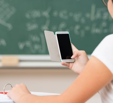 Symbolbild: Schülerin im Klassenraum mit Handy in der Hand