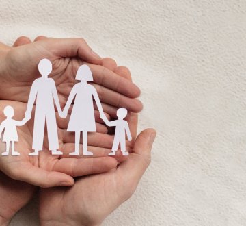 Symbolbild: Gefaltete Hände, die ausgeschnittene Figuren einer Familie aus Vater, Mutter, zwei Kindern halten